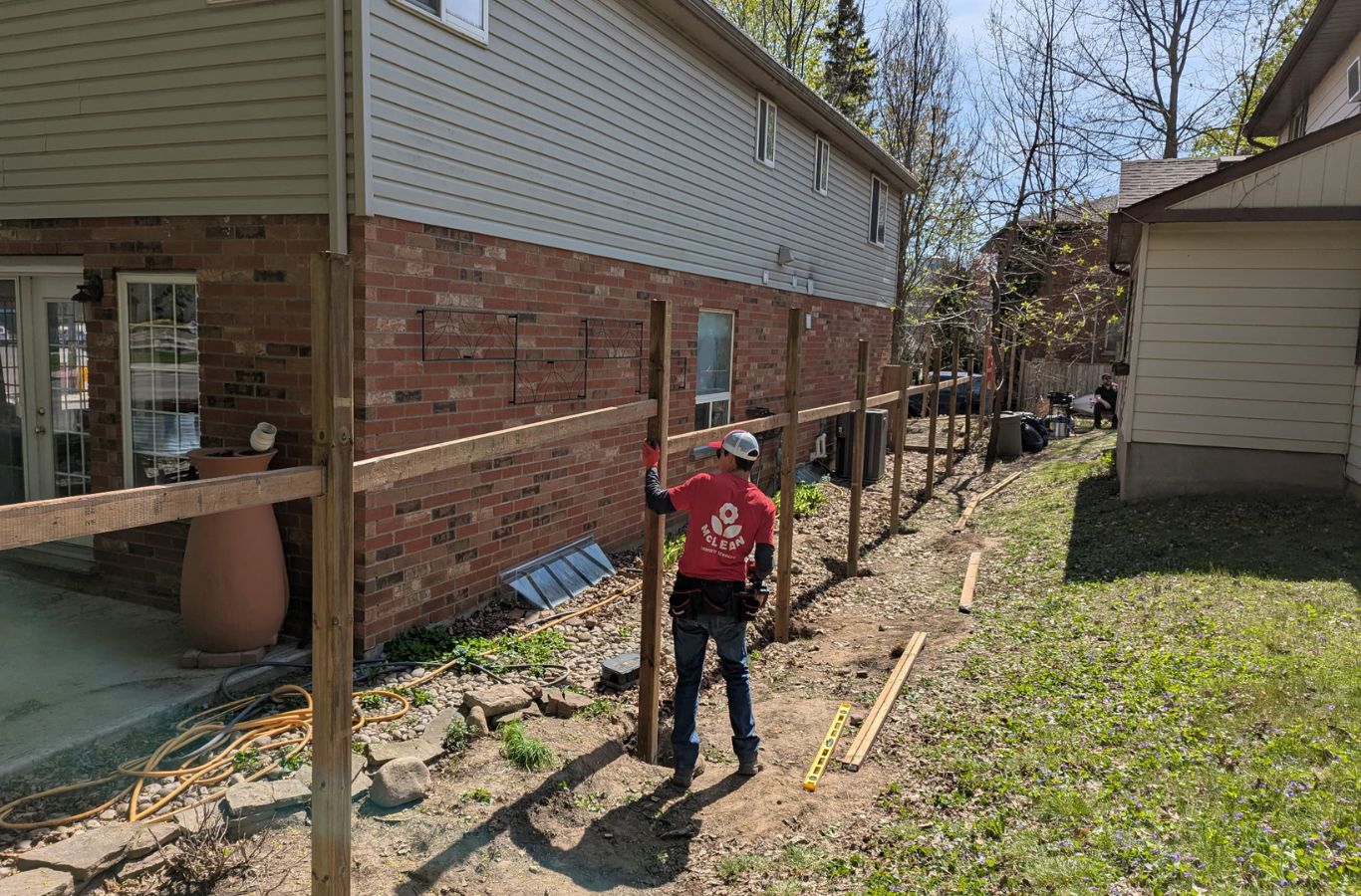 Technician performing Fence Post Repair beside a sloped yard fence in Elora - ON with leveling tools. Fence Post Repair near me.